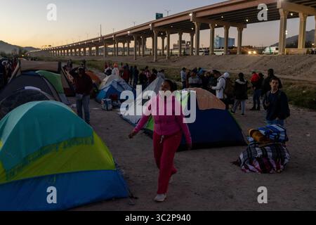 I migranti navigano in un campo tenda sotto un cavalcavia dell'autostrada di Ciudad Juarez al crepuscolo, riflettendo le sfide in corso al confine tra Stati Uniti e Messico. Foto Stock