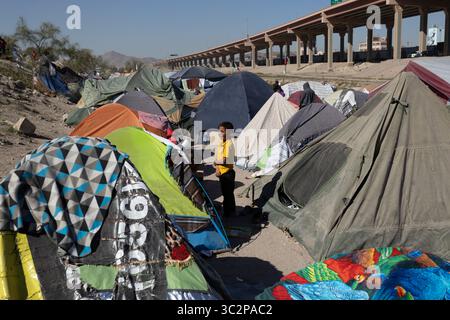 Un ragazzo si trova tra tende vivaci in un campo di migranti improvvisato sotto un'autostrada a Ciudad Juarez, evidenziando le sfide in corso affrontate dai migranti al confine tra Stati Uniti e Messico. Foto Stock