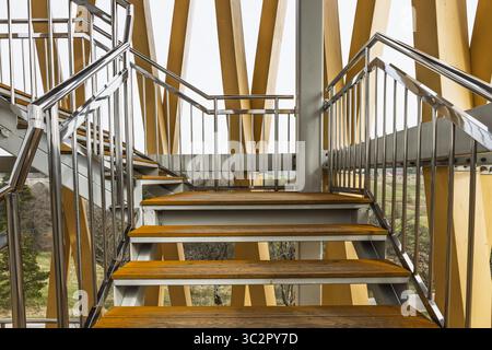 Vista prospettica verso l'alto della scala in legno laminato sostenibile con eleganti ringhiere in metallo Foto Stock