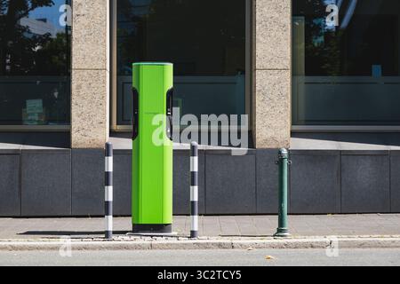 Stazione di ricarica EV verde brillante su un marciapiede della città vicino a un ufficio Foto Stock