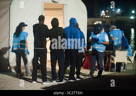 5 agosto 2019, Malaga, Spagna: I migranti sono visti in fila fuori da una tenda della Croce Rossa spagnola in quanto vengono identificati da un membro dell'Agenzia europea della Guardia di frontiera e costiera (Frontex) dopo il loro arrivo al porto di Malaga. Il servizio di soccorso marittimo spagnolo ha salvato un totale di 96 migranti (di cui 10 donne e 9 migranti maghrebin) a bordo di due gommoni che attraversavano il mare di Alboran e li ha portati al porto di Malaga, dove sono stati assistiti dalla Croce Rossa spagnola. Secondo fonti governative spagnole, il numero di migranti che cercano di raggiungere le coste spagnole nel 2019 è sceso del 40,2% Foto Stock