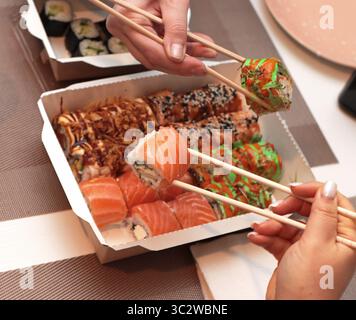 Un invitante shot di sushi roll disposti elegantemente su un tavolo. Mani delicate con bacchette, che mettono in mostra l'arte della cena. Nelle vicinanze, tovaglioli Foto Stock