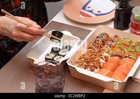 Un invitante shot di sushi roll disposti elegantemente su un tavolo. Mani delicate con bacchette, che mettono in mostra l'arte della cena. Nelle vicinanze, tovaglioli Foto Stock