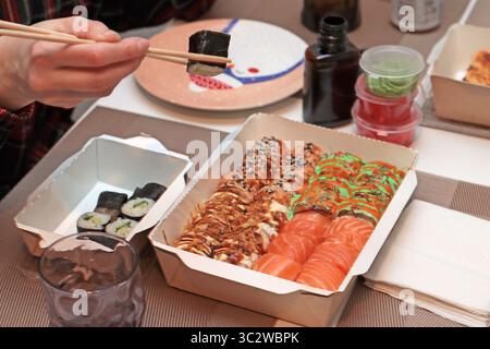 Un invitante shot di sushi roll disposti elegantemente su un tavolo. Mani delicate con bacchette, che mettono in mostra l'arte della cena. Nelle vicinanze, tovaglioli Foto Stock