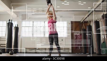 Donna di mezza età in cima rosa che solleva pesanti campanelli in palestra, sacchetti di pugno, sovrapposizioni dati Foto Stock