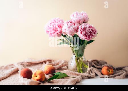 Natura morta con fiori di peonia in vaso e frutti di pesca in tavola. Foto Stock