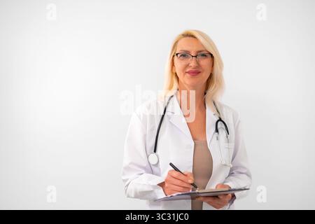 Donna matura, medico, terapista o medico di famiglia sorridente, vestita con un camice da laboratorio con stetoscopio, su sfondo bianco pulito. Spazio di copia per gli annunci sanitari Foto Stock