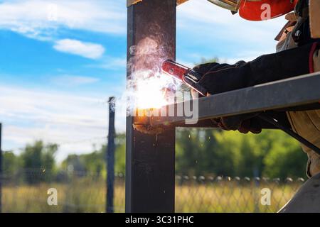 Una saldatrice con indumenti protettivi lavora su una struttura metallica all'aperto Foto Stock