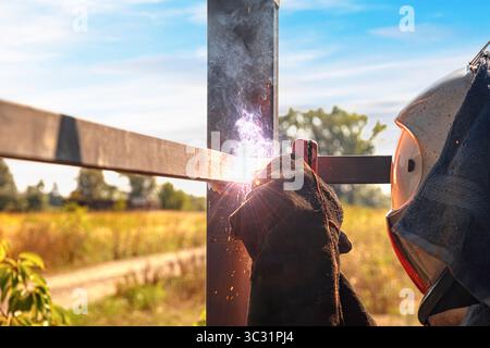 Una saldatrice con indumenti protettivi lavora su una struttura metallica all'aperto Foto Stock