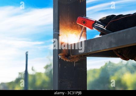 Una saldatrice con indumenti protettivi lavora su una struttura metallica all'aperto Foto Stock