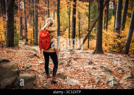 Donna in abbigliamento sportivo, escursionismo all'aperto. Escursionista in solitaria con zaino rosso che si gode un'escursione nella foresta autunnale Foto Stock