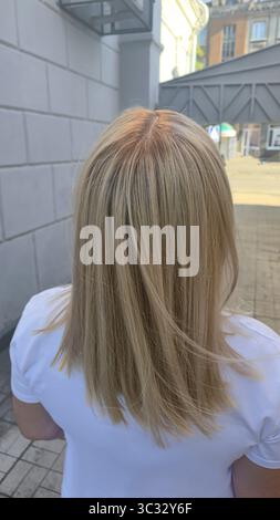 Donna con lunghi capelli tinti leggeri in piedi in un salone di bellezza con schiena. Bionda. Paralume di cenere. Foto Stock