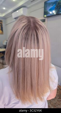 Donna con lunghi capelli tinti leggeri in piedi in un salone di bellezza con schiena. Bionda. Paralume di cenere. Foto Stock