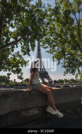 Donna seduta sul muro che guarda la Torre Eiffel il giorno d'estate a Parigi. Foto Stock