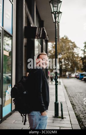 Uomo con zaino che sorride sul marciapiede della città Foto Stock