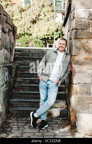 Uomo sorridente davanti a un vecchio muro di pietra in autunno Foto Stock
