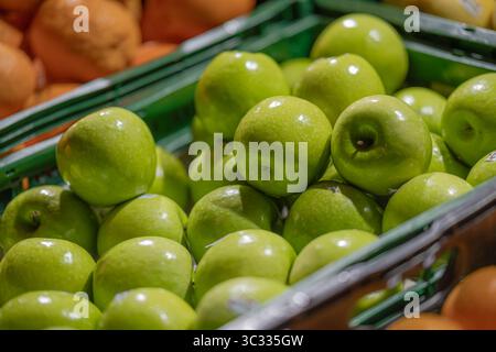 Vista dall'alto di una cassa di mele verdi in un negozio di alimentari, con arance sullo sfondo. Le mele appaiono fresche e lucide. Foto Stock