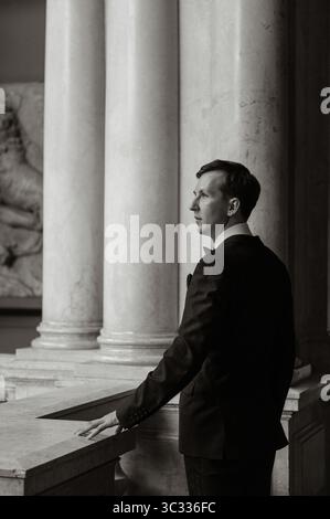 Un uomo elegante in abbigliamento formale si trova vicino a colonne di marmo Foto Stock
