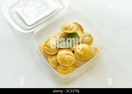 Una deliziosa serie di polpette preparate al momento disposte in modo ordinato in un contenitore di plastica trasparente con foglie di alloro e spezie pronte per la cottura o il servizio Foto Stock