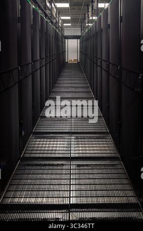 Corridoio scuro della sala server con pavimento in griglia metallica e armadietti per server, che mettono in risalto l'infrastruttura del data center Foto Stock