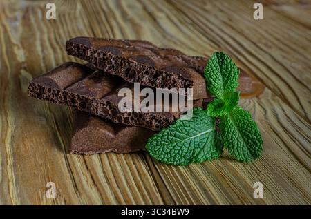 Uno shot ravvicinato di due pezzi di cioccolato fondente poroso, uno impilato sull'altro, con foglie di menta verde fresca accanto a loro su uno sfondo rustico in legno Foto Stock
