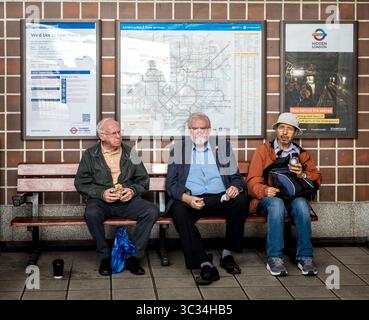 Tre passeggeri seduti in panchina nella stazione della metropolitana di Acton Town, Londra, Regno Unito Foto Stock