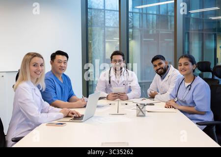 Un gruppo eterogeneo di medici professionisti sono seduti intorno a un tavolo da conferenza, sembra essere in discussione e collaborare. Foto Stock