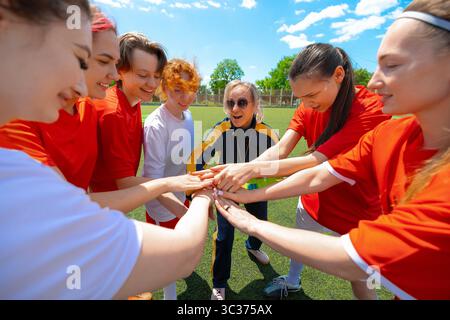 La squadra di calcio femminile e l'allenatore femminile si uniscono per mano in un guazzabuglio prima della partita sul campo soleggiato Foto Stock