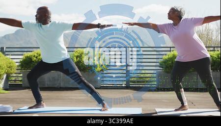 Una coppia che indossa un abbigliamento sportivo e posa il guerriero II sulla terrazza, con interfaccia digitale Foto Stock
