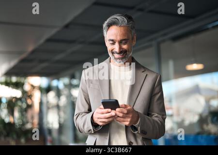 Uomo d'affari felice e maturo in piedi all'aperto con il telefono cellulare. Foto Stock