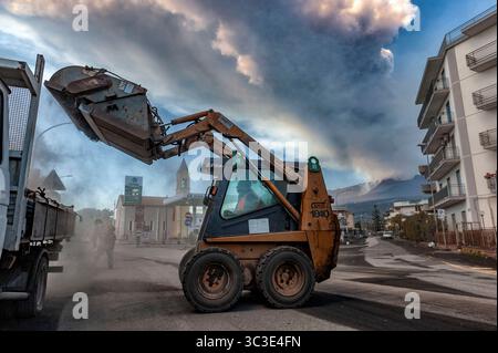 12 marzo 2021 - Mascali, Catania, Italia - comune di Mascali, località Fondachello, Valle dell'Etna, Sicilia. Diversi lavoratori lavorano con i loro mezzi per ripulire il paese da una fitta coperta di sabbia vulcanica caduta a seguito dei vari parossismi verificatisi tra gennaio e marzo 2021. Mentre gli uomini lavorano avvolti dalla polvere, dietro di loro il vulcano si è risvegliato con un'altra violenta eruzione. (Immagine di credito: © Vito Finocchiaro/ZUMA Wire) Foto Stock