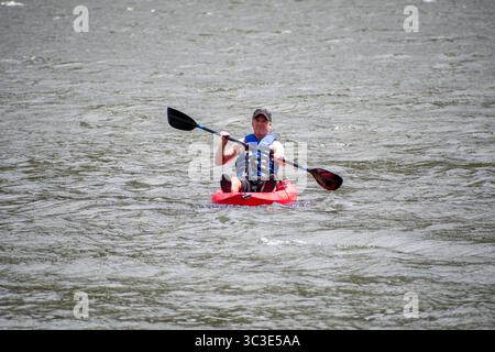 Summit County, Utah - 20 luglio 2025: Un uomo pagaia su un kayak rosso brillante a Smith and Morehouse Reservoir. Foto Stock