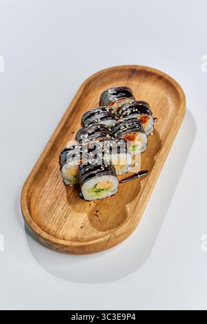 Deliziosi sushi roll disposti su un piatto di legno, con ingredienti freschi e colori vivaci, perfetti per un pasto gourmet o un pranzo informale Foto Stock