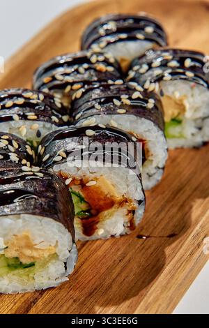 Deliziosi Sushi Rolls disposti ad arte su un piatto di legno, con ingredienti freschi e allettanti presentazioni per una delizia culinaria Foto Stock