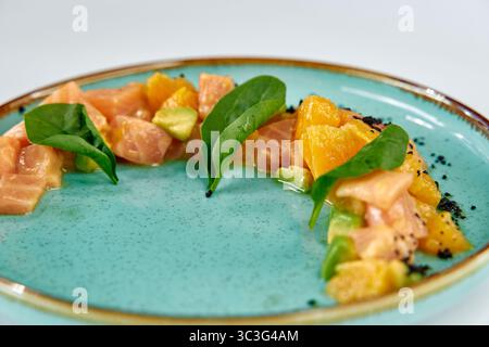 Una vivace e artistica presentazione della tartare di salmone, con ingredienti freschi come agrumi e spinaci su un piatto dai colori meravigliosi Foto Stock