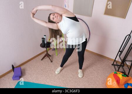 Una donna adulta esegue una curva laterale dinamica, le braccia sollevate in una postura perfetta, come parte di una routine di fitness domestica rinvigorente. Lunghezza completa di 44 anni-olo Foto Stock