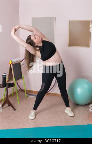 Vista a tutta lunghezza di una donna adulta che esegue una curva laterale dinamica, con le braccia sollevate in una postura perfetta, segmento della routine domestica pilates. Wo Foto Stock