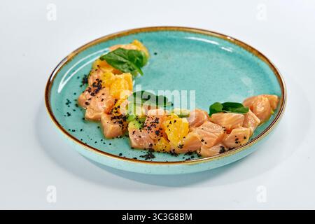 Un piatto di salmone fresco e colorato, preparato ad arte con segmenti di arancia e verdi a foglia su un vivace piatto Aqua perfetto per presentazioni culinarie Foto Stock