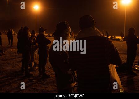 I migranti si riuniscono di notte al confine di Ciudad Juarez, discutendo e aspettando. Foto Stock