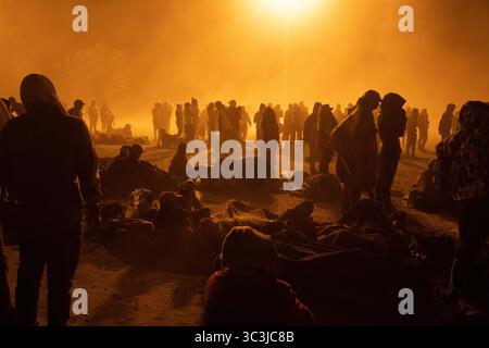 I migranti che si stagliano si riuniscono sotto una luce arancione sul confine di Ciudad Juarez di notte. Foto Stock