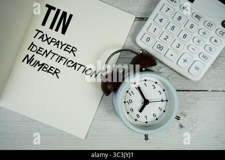 Testo del numero di identificazione del contribuente su un foglio di carta con sveglia e calcolatrice su sfondo in legno Foto Stock