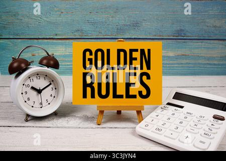 Testo delle regole d'oro scritto su carta con calcolatrice e sveglia su sfondo di legno Foto Stock