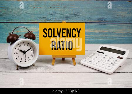 Testo del rapporto di solvibilità scritto su carta con calcolatrice e sveglia su sfondo in legno Foto Stock