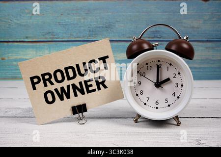 Testo del proprietario del prodotto scritto su carta con sveglia su sfondo in legno Foto Stock