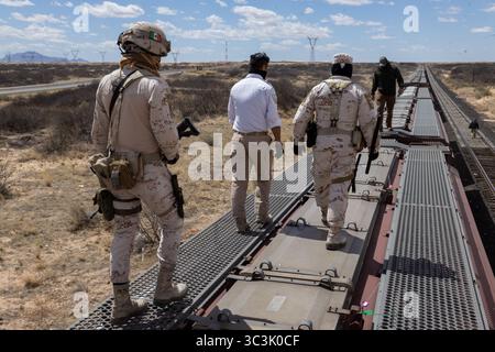 Le forze armate monitorano un treno merci in un deserto vicino a Ciudad Juarez, supervisionando le rotte dei migranti con turbine eoliche visibili. Foto Stock