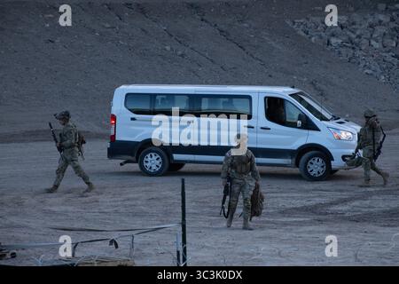 Soldati armati pattugliano un deserto roccioso vicino a Ciudad Juarez al crepuscolo, monitorando i valichi di frontiera e le attività di immigrazione. Foto Stock