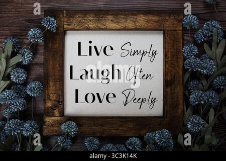 Vivi semplicemente ridi spesso ama profondamente il testo con decorazioni floreali su sfondo in legno Foto Stock