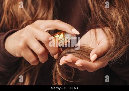 Donna che applica siero per capelli. Mani con trattamento a olio. Concetto di routine per la cura dei capelli. Lunghi capelli castani sani. Rituale di bellezza naturale. Capelli idratanti. Foto Stock