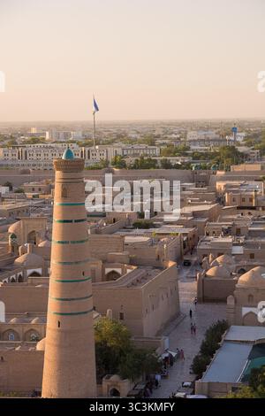 Khiva, Uzbekistan - 12 luglio 2024: Veduta aerea del minareto Pahlavon Mahmud con sullo sfondo la storica città di Khiva e una bandiera uzbeka che sventola i Foto Stock