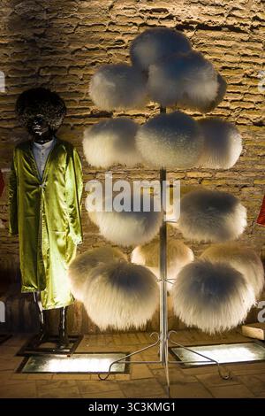 Khiva, Uzbekistan - 12 luglio 2024: Foto notturna di una mostra di tradizionali cappelli di pelliccia bianca nella città di Khiva, Uzbekistan, illuminati da luci calde Foto Stock